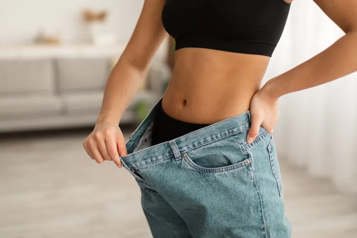 liposuction - Charm City Plastic Surgery - Charm City Plastic Surgery a woman stretching out her jeans to show the weight loss after liposuction treatment