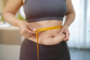 tummy-tuck-cost - Charm City Plastic Surgery Woman preparing for tummy tuck procedure and measuring her waist