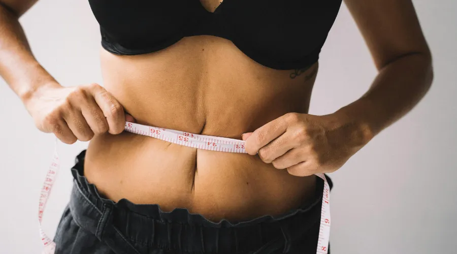 Person in a black sports bra measuring their waist with a tape measure for fitness or weight loss.