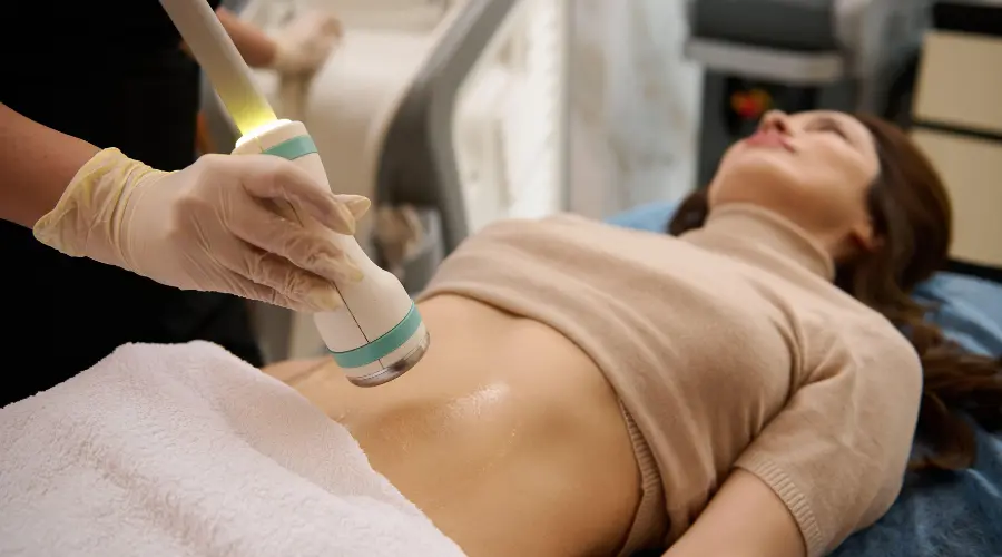Medical professional in gloves using a handheld device on a patient's abdomen during a non-invasive treatment.