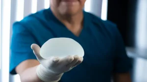 Gloved hand holding a silicone breast implant in a clinical setting, ready for a procedure.