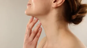 Close-up side profile of a woman's neck and jawline as she lightly touches her throat with her fingers.